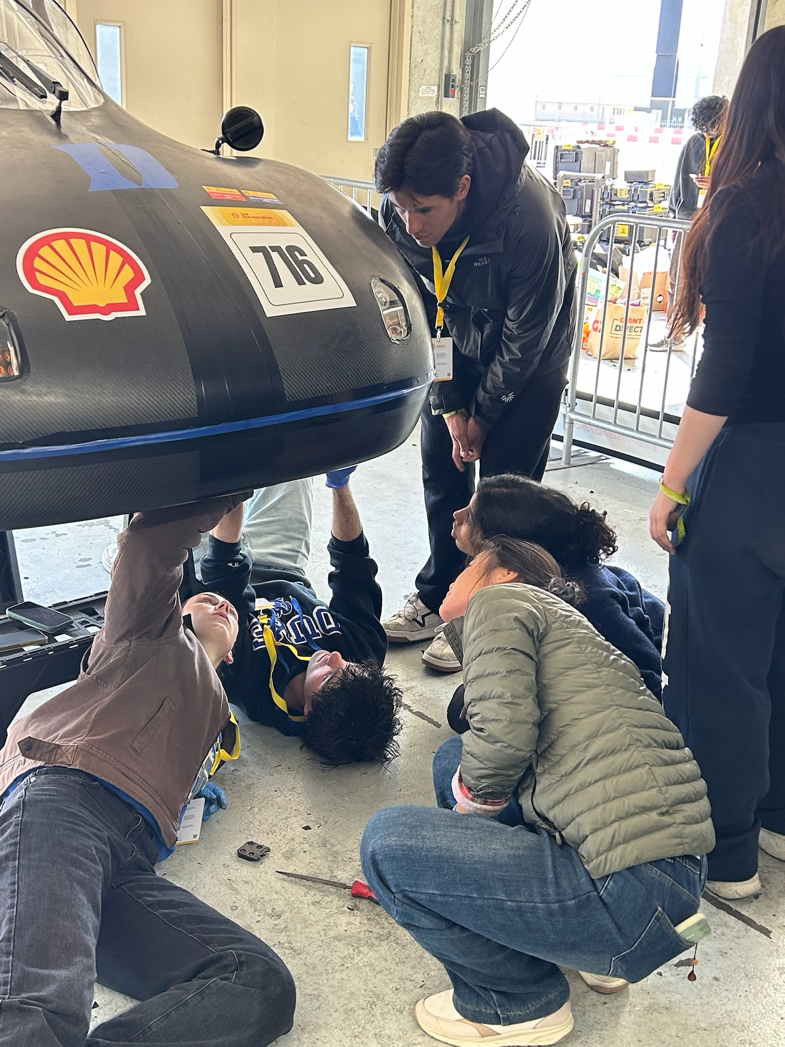 Team members shoulder to shoulder under the raised car during competition