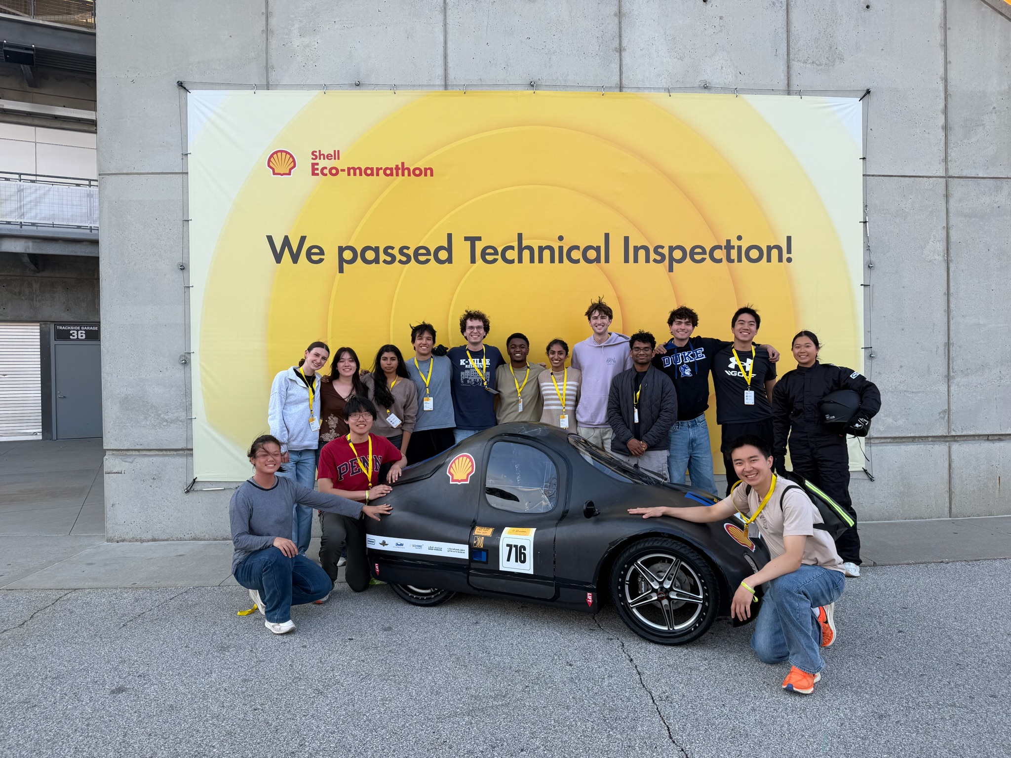 Team members leaning on car 716 in front of the technical inspection banner
